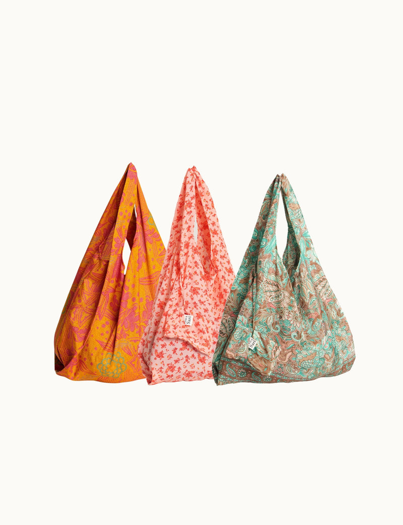 Set of three reusable fabric bags with floral and paisley patterns in orange, pink, and teal, hanging side by side