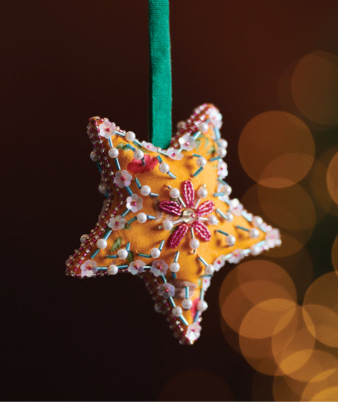 Yellow fabric star ornament with pink and white bead and floral embroidery, hanging from a green ribbon