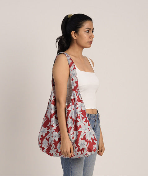 Woman wearing a red trapeze bag with large white floral print over her shoulder, side view, paired with white top and blue jeans