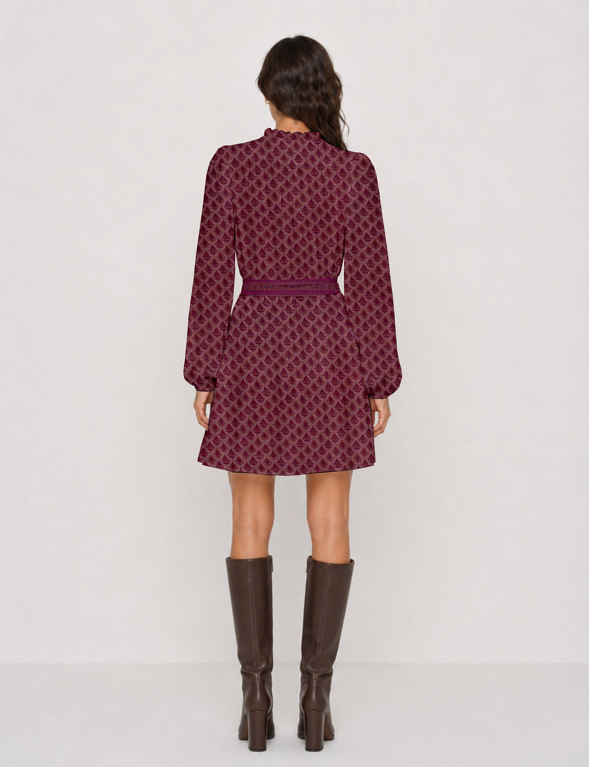 Woman wearing a pink swing dress with a leaf pattern, long sleeves, a belt at the waist, and brown knee-high boots, back view