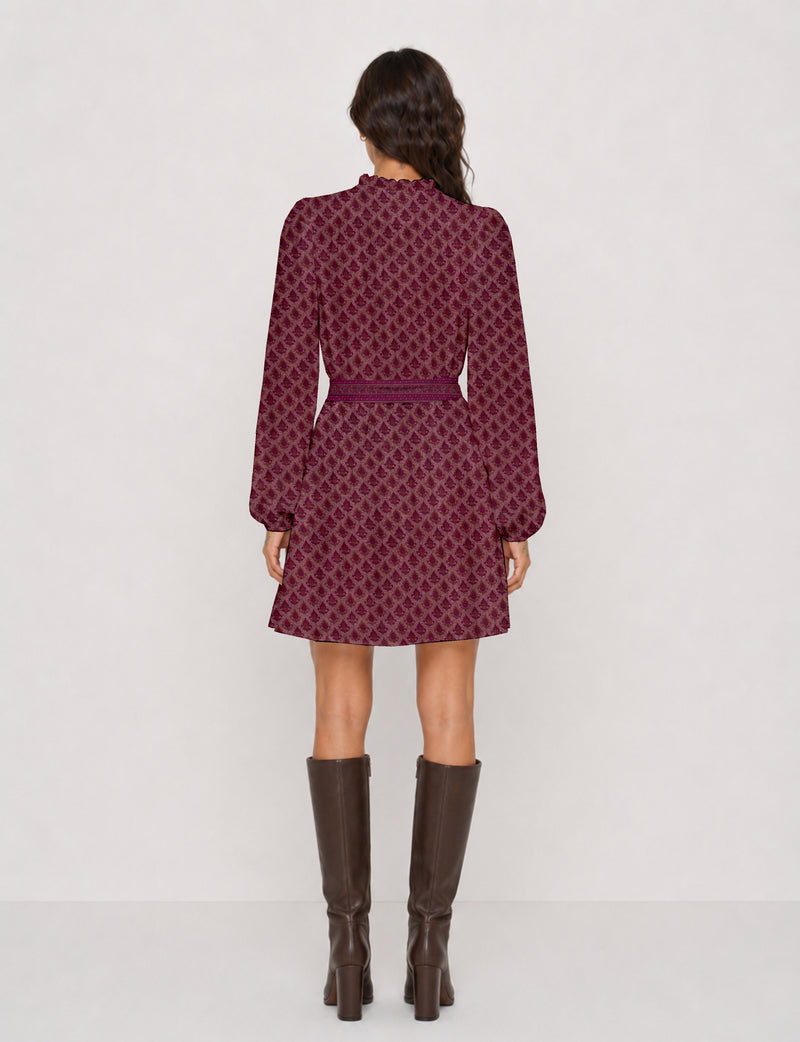 Woman wearing a pink swing dress with leaf pattern, long sleeves, scalloped neckline, and matching belt, shown from back