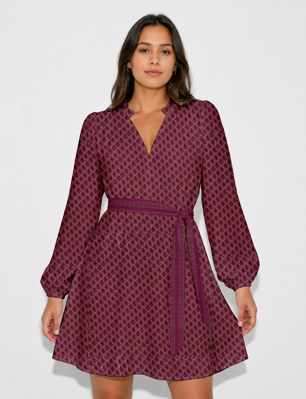 Woman wearing a pink swing dress with leaf pattern, long puff sleeves, scalloped V-neckline, and matching belt, front view