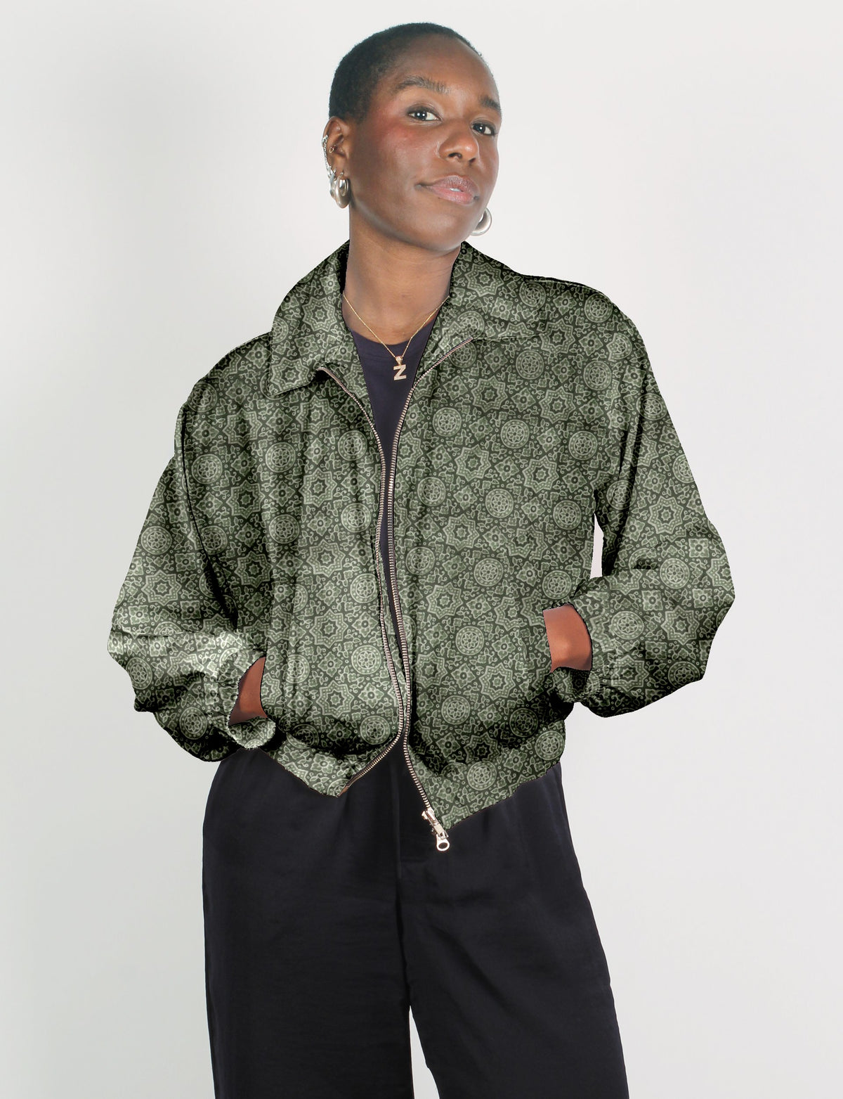 Green bomber jacket with Indian ethnic pattern, front zipper, collar, and elastic cuffs, worn by model with hands in pockets