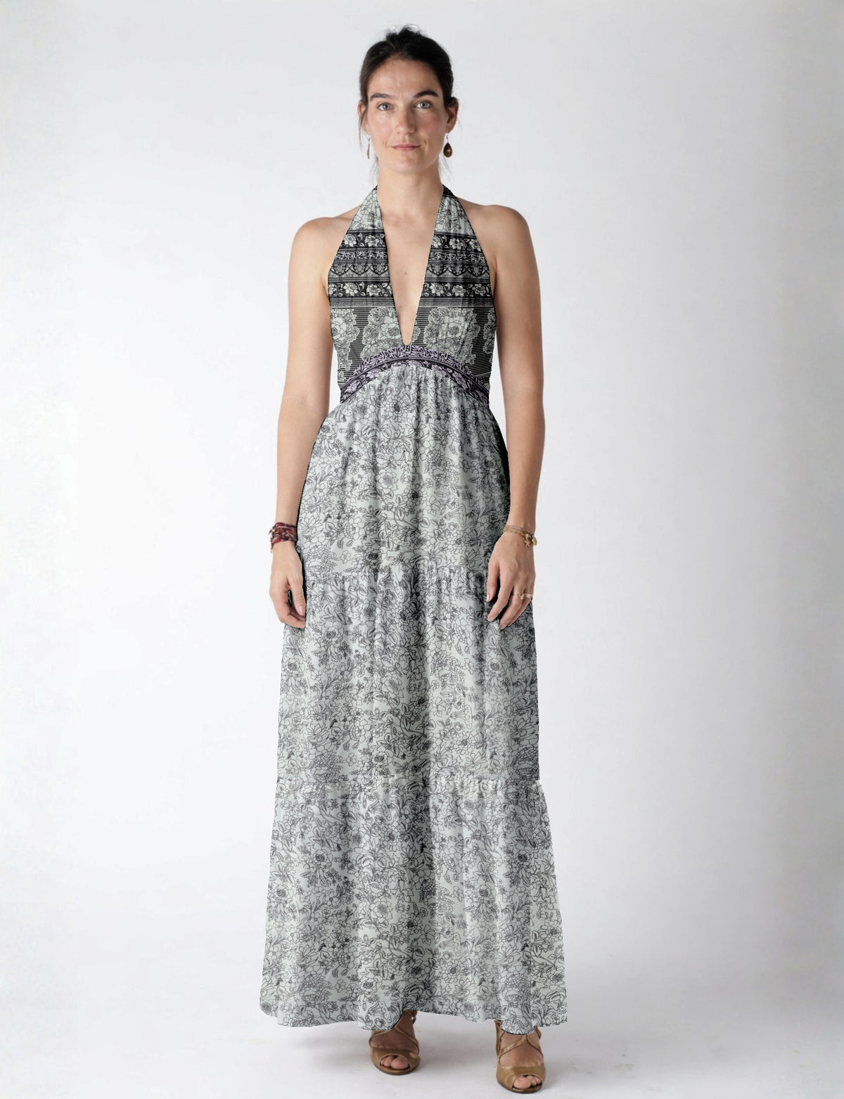 Woman wearing a white maxi tiered dress with black floral and stripe patterns, halter neckline, and deep V front view