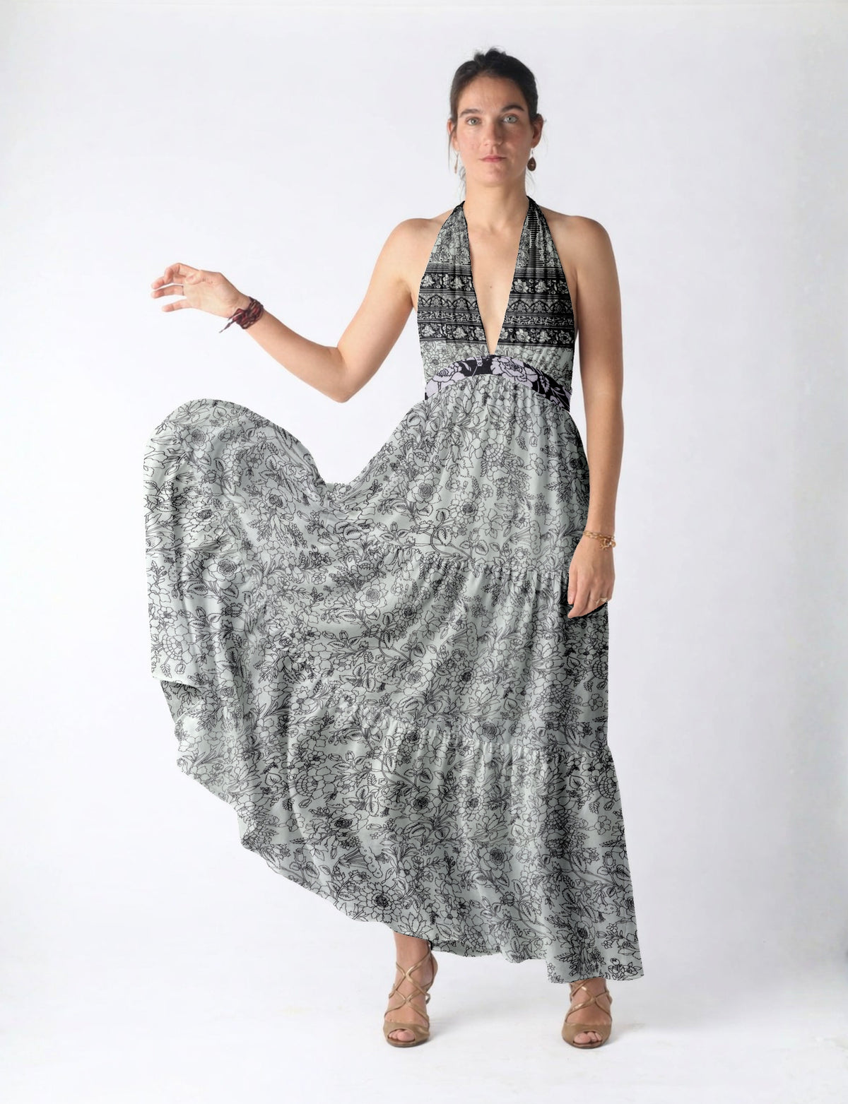 Woman wearing a white maxi tiered dress with black floral and geometric patterns, halter neckline, and beige strappy heels