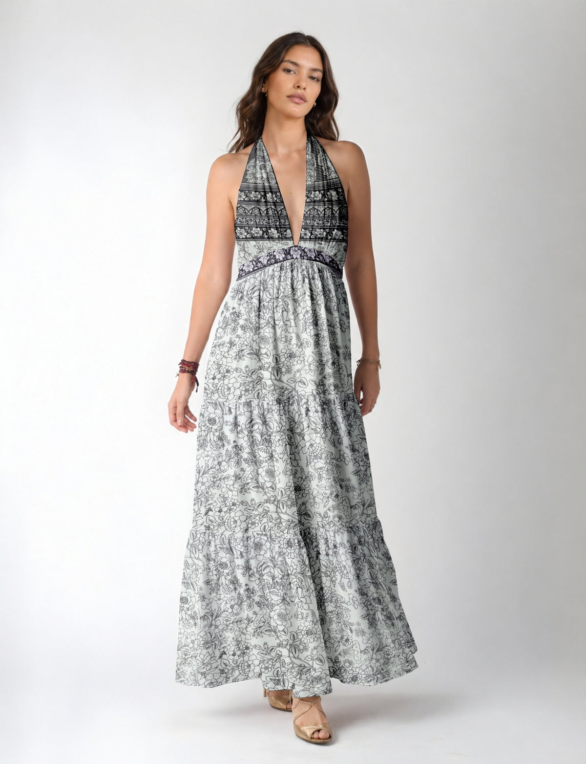 Woman wearing a white maxi tiered dress with black floral and geometric patterns and a deep V halter neckline, front view