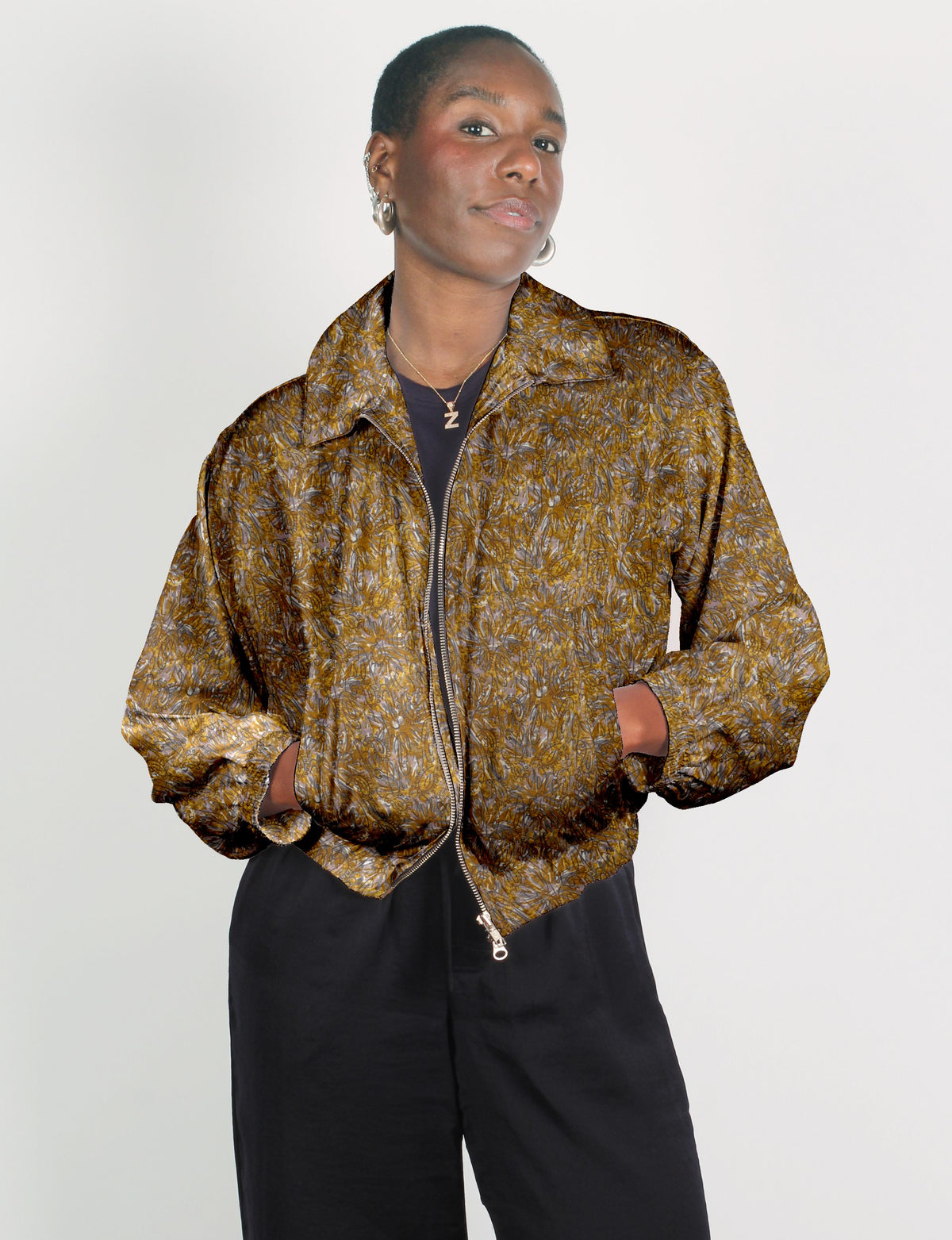 Model wearing a yellow and brown abstract patterned bomber jacket with front zipper and elastic cuffs, paired with black