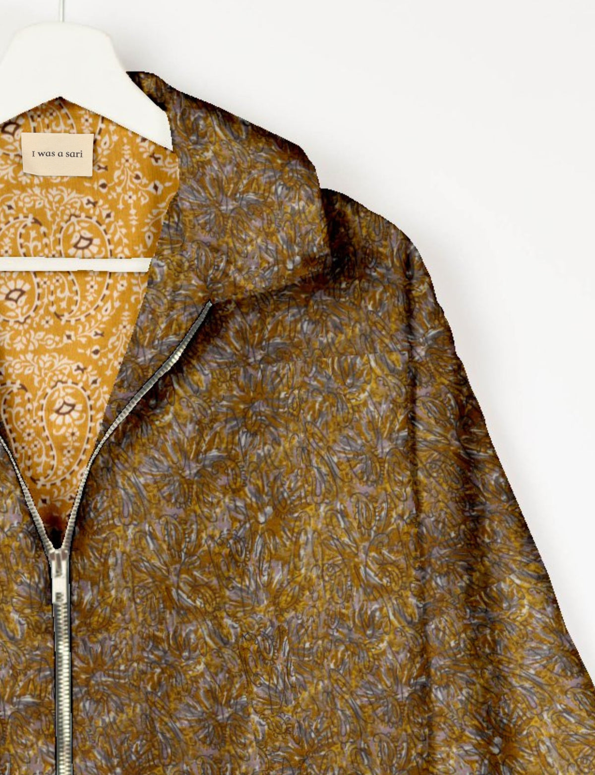 Yellow and brown abstract patterned bomber jacket with silver zipper, hanging on white hanger, label reads "I was a sari"