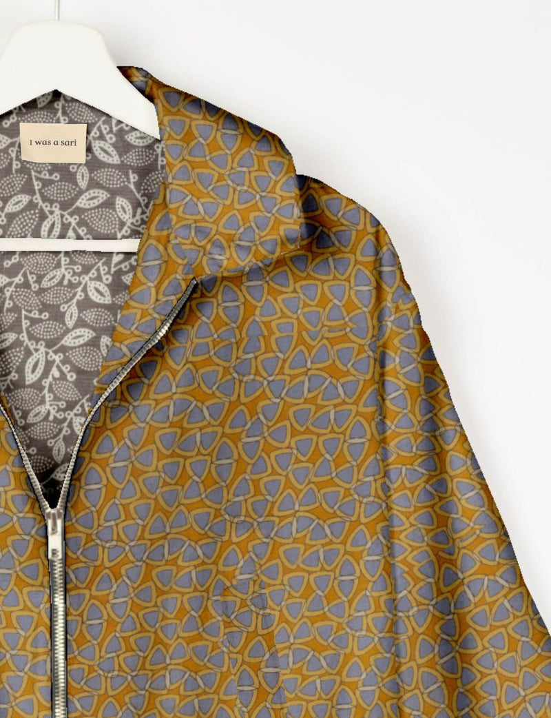 Yellow bomber jacket with blue geometric pattern, silver zipper, and gray floral patterned lining on white hanger