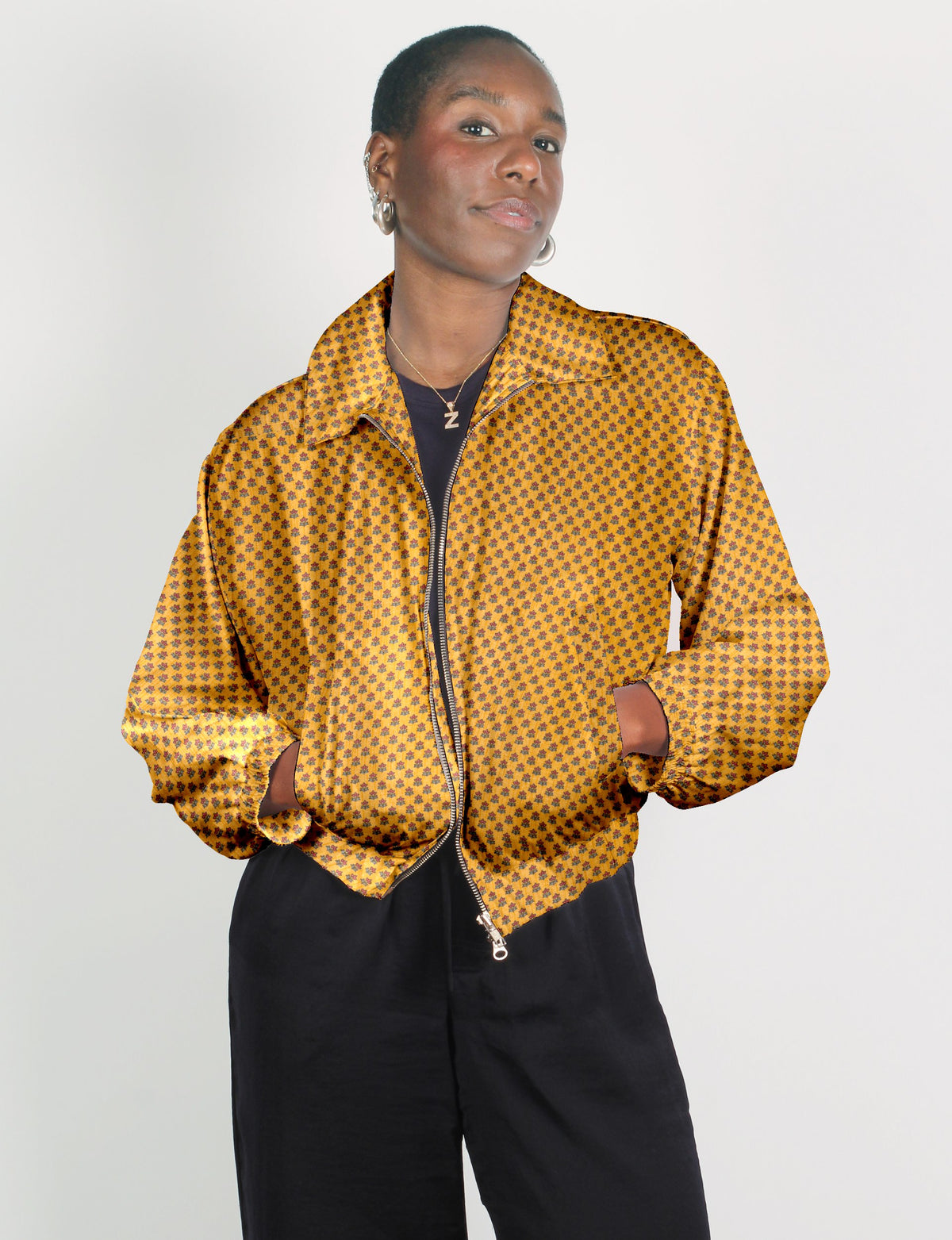 Woman wearing a yellow bomber jacket with small dark floral micro design, front zipper, and elastic cuffs, paired with black