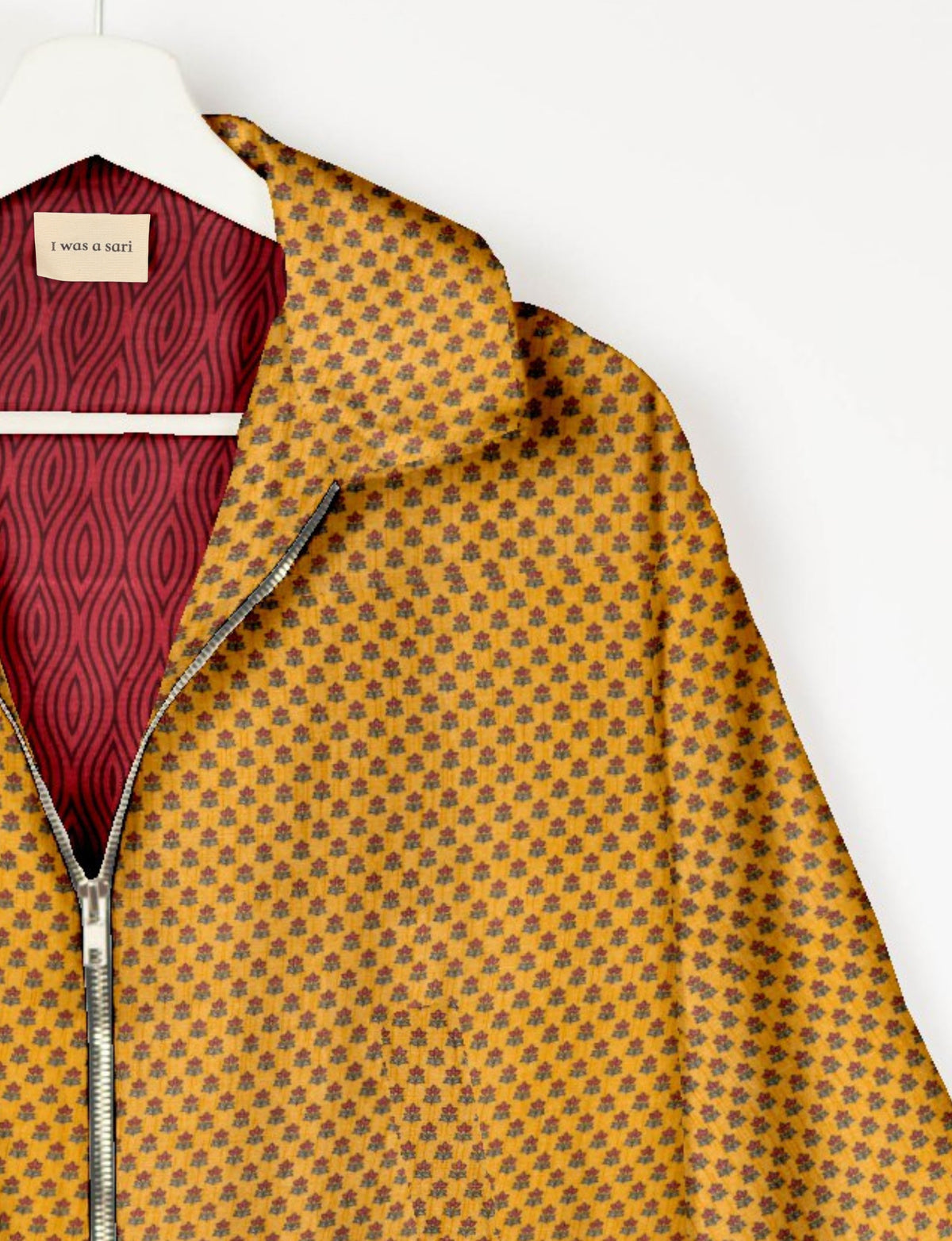 Yellow bomber jacket with small floral pattern, silver zipper, and red patterned inner lining labeled "I was a sari" on