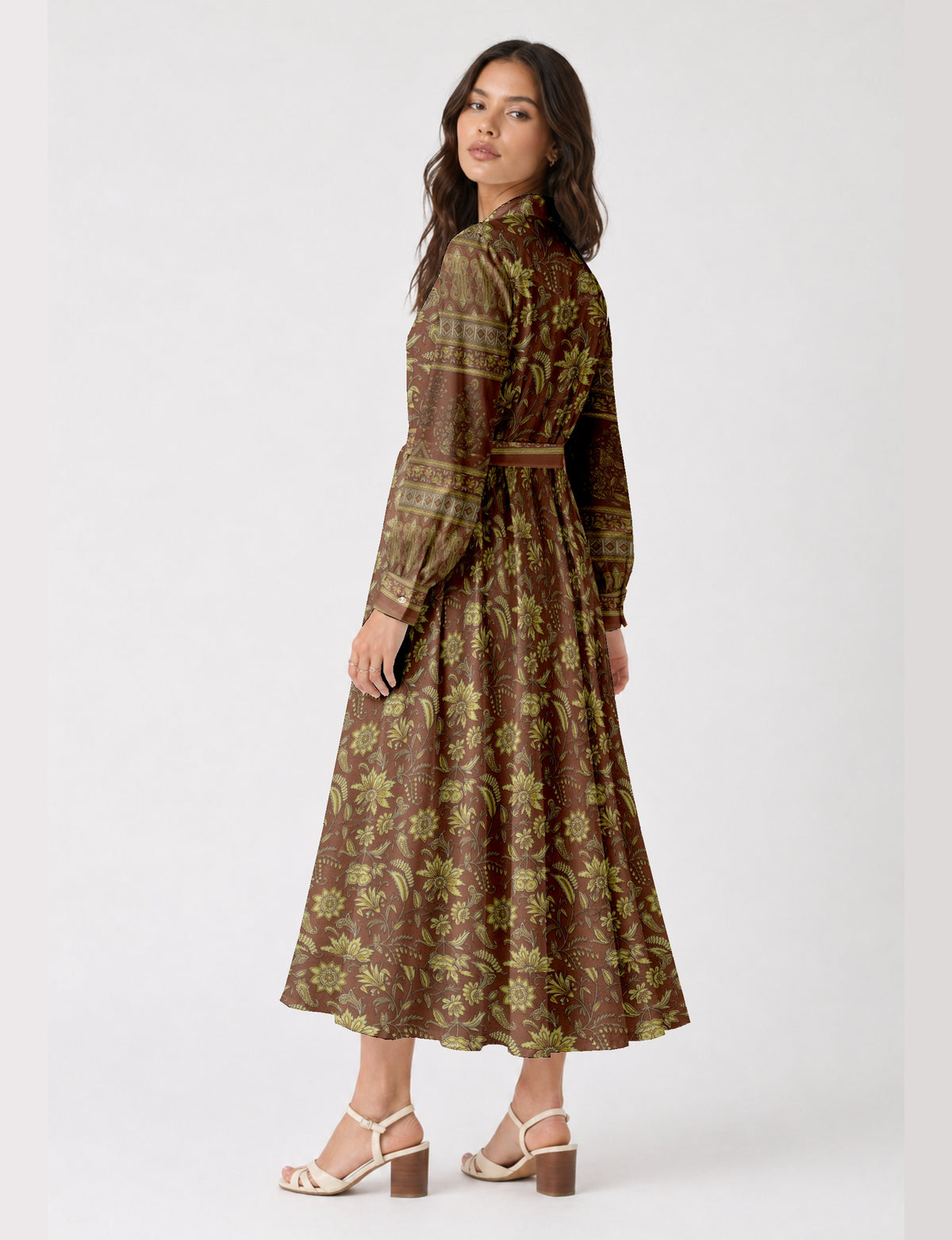 Woman wearing a brown long shirt dress with yellow floral and paisley print, long sleeves, and a belted waist, back view