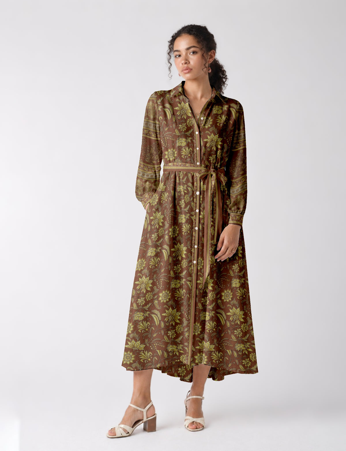 Long brown shirt dress with yellow floral print, button front, long sleeves, and waist tie, worn by model standing