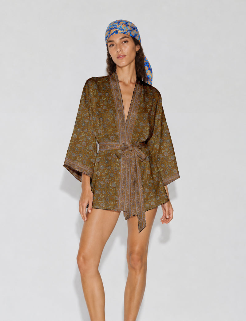 Woman wearing a short brown floral kimono robe with wide sleeves and a matching belt, paired with a blue and orange