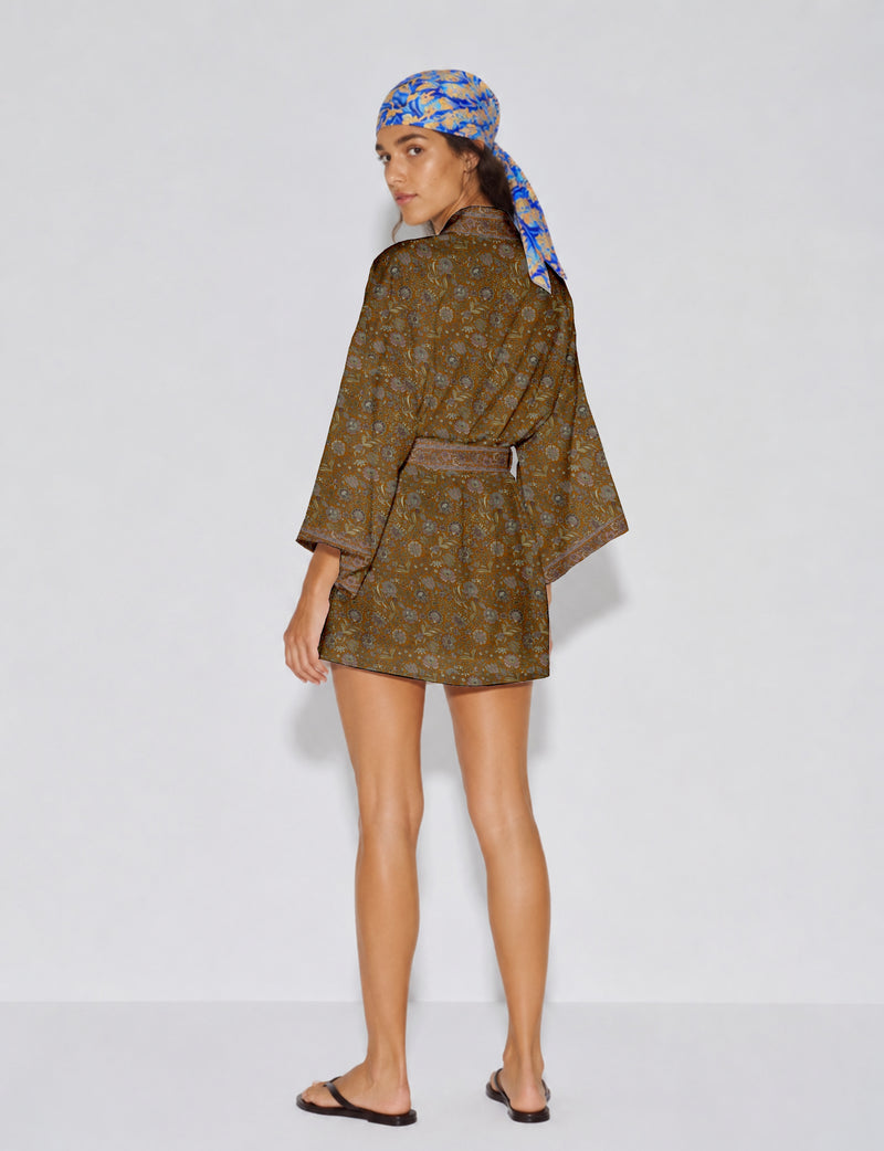 Woman wearing short brown floral kimono robe with wide sleeves and matching belt, paired with blue and yellow patterned