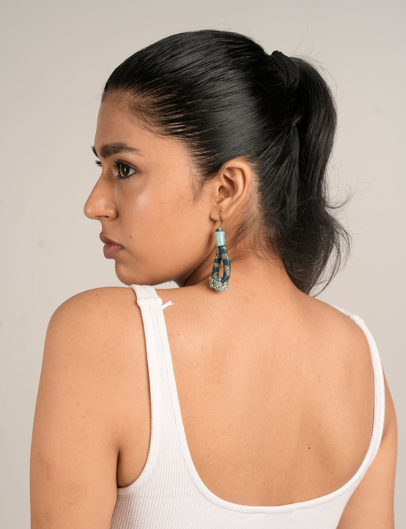 Woman wearing blue and gold beaded drop earrings with floral pattern, side view, white ribbed tank top visible from back
