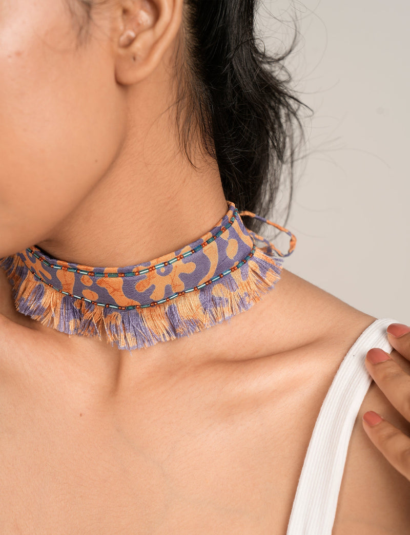 Yellow and purple abstract patterned fabric fringe choker with blue and orange bead details, worn by model front side view