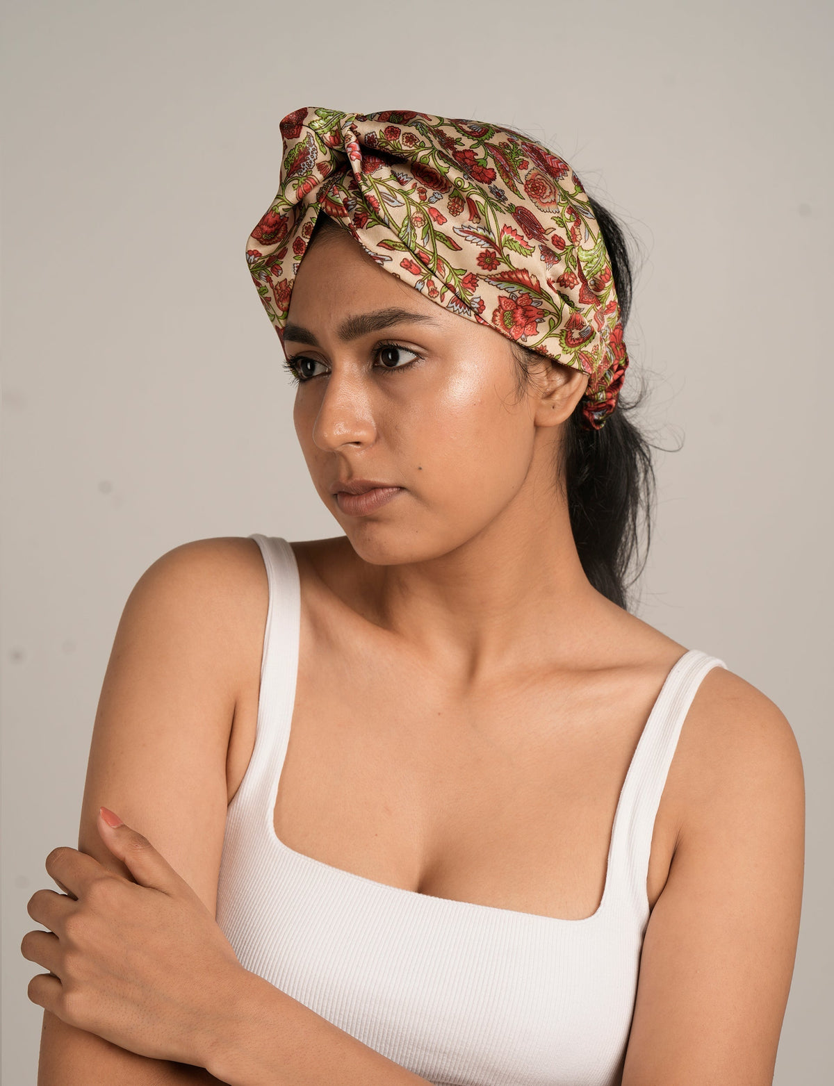 Woman wearing a pink floral patterned turban headband with green and red details, shown in close-up side view