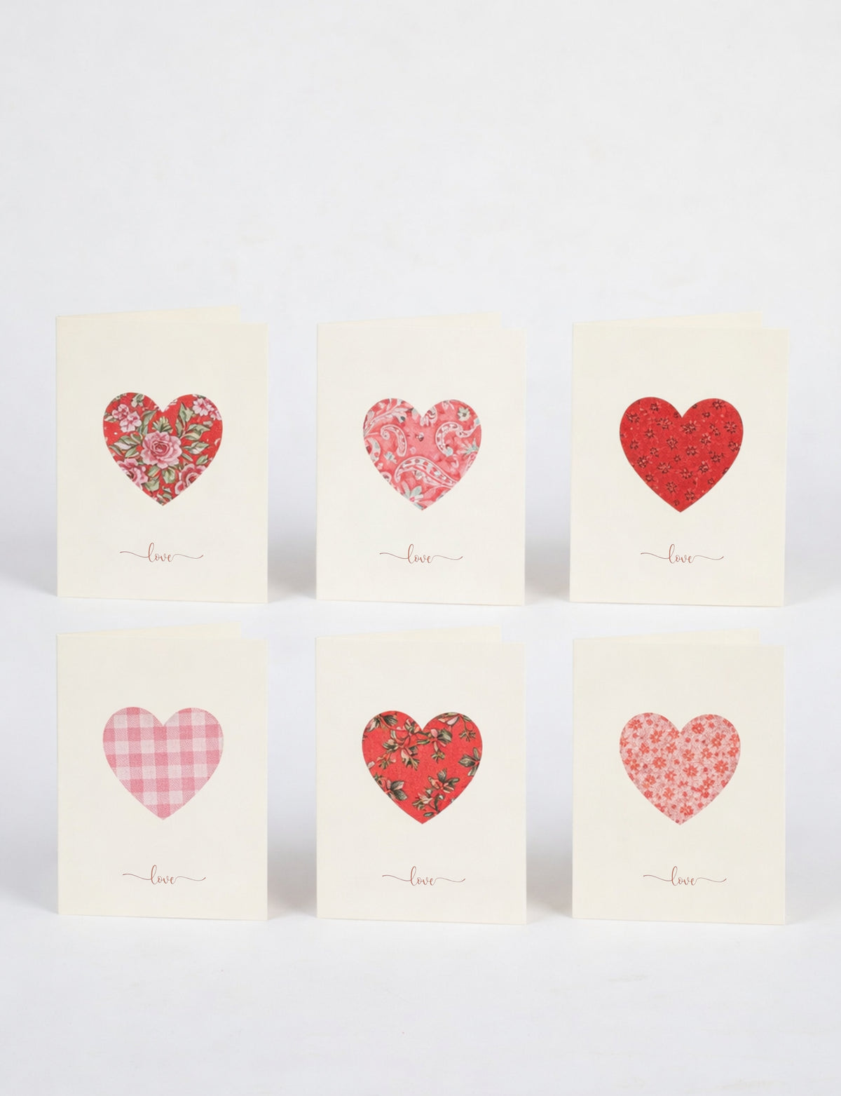 Set of six cream folded celebration cards with assorted red and pink patterned heart cutouts and "love" text below each heart