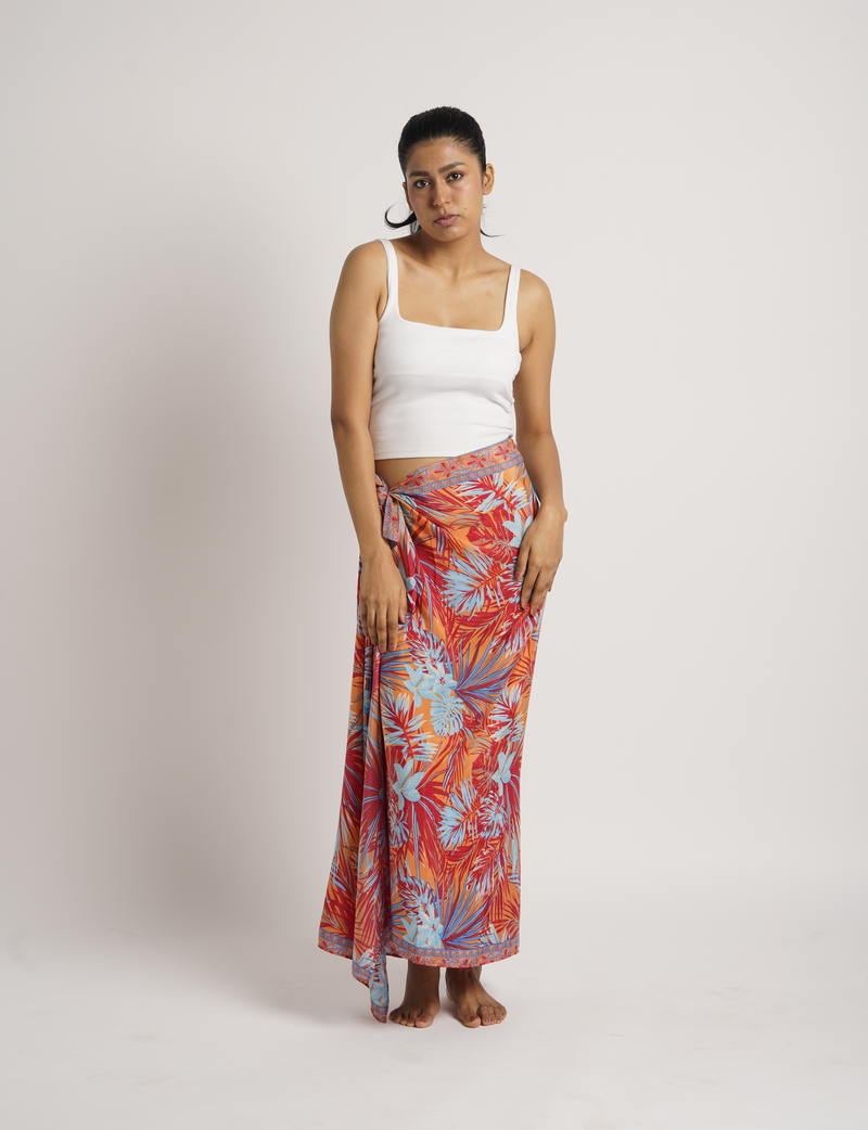 Woman wearing a pink geometric patterned pareo tied at the waist, paired with a white sleeveless crop top, front view