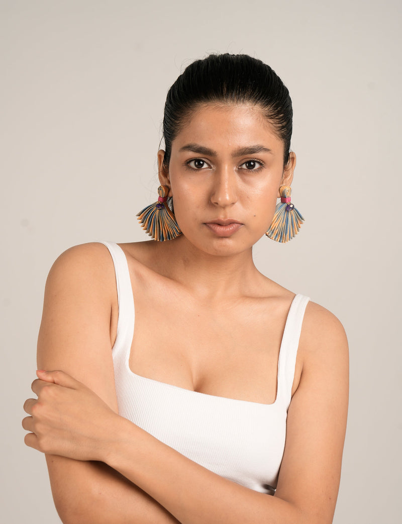 Model wearing pleated fan-shaped earrings with green, blue, and orange abstract pattern, front view, neutral background