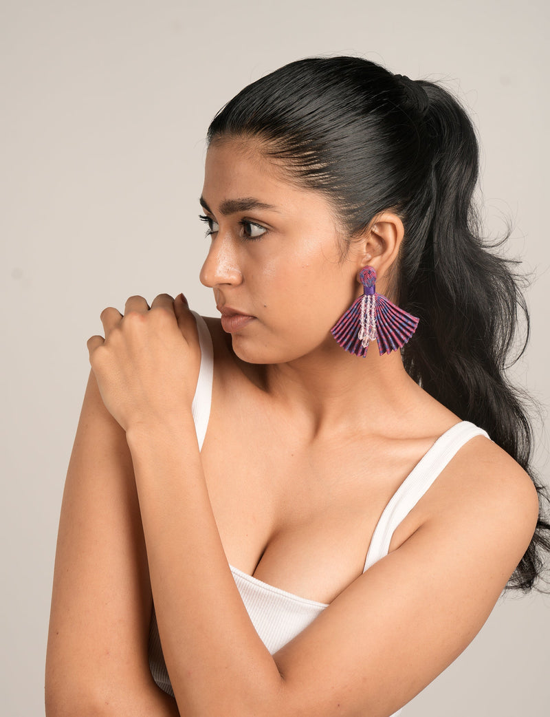 Model wearing pleated pink and purple abstract patterned earrings with clear bead tassels, side view on neutral background
