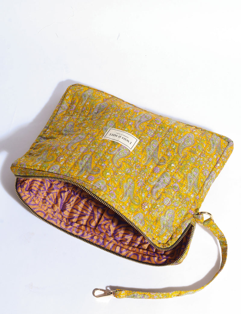 Quilted yellow paisley organizer with purple patterned interior, zipper closure, and detachable wrist strap, flat lay view