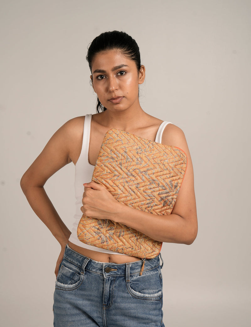 Woman wearing white tank top and blue jeans holding a yellow floral quilted laptop sleeve in front view