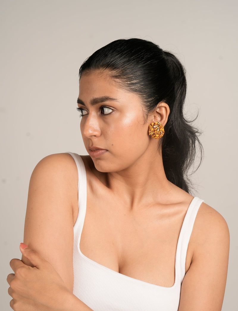 Woman wearing yellow ruffle fabric earrings with a textured pattern, shown in close-up side view with white tank top