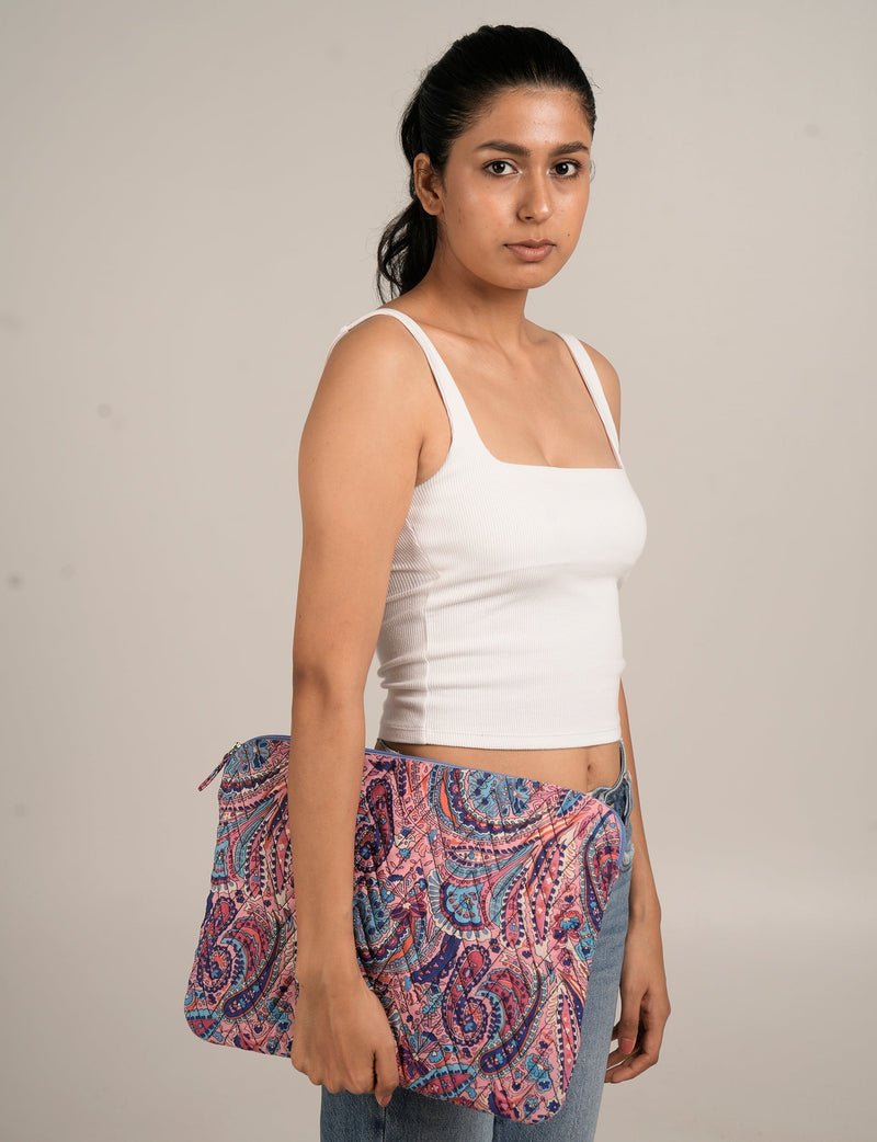 Woman holding a purple paisley quilted laptop sleeve with zipper, wearing white tank top and blue jeans, side view