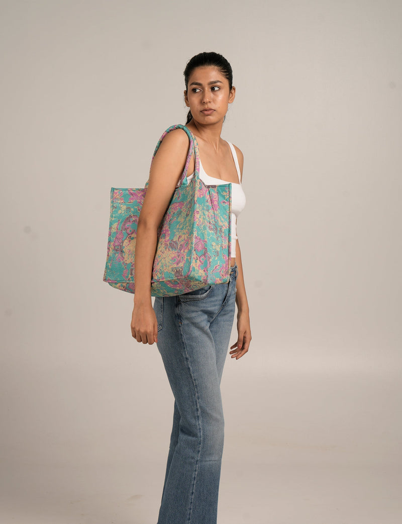 Woman wearing a white tank top and jeans carrying a large purple and teal floral patterned tote bag on her shoulder
