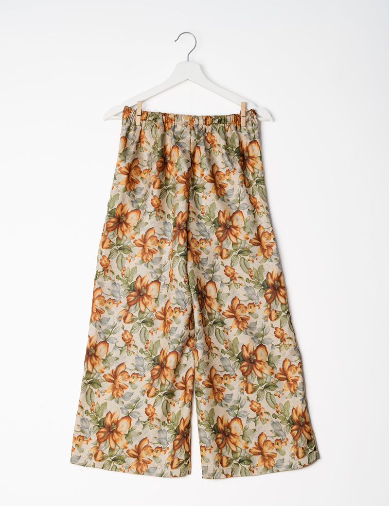 Beige floral print wide-leg pants with elastic waistband hanging on white hanger against white background
