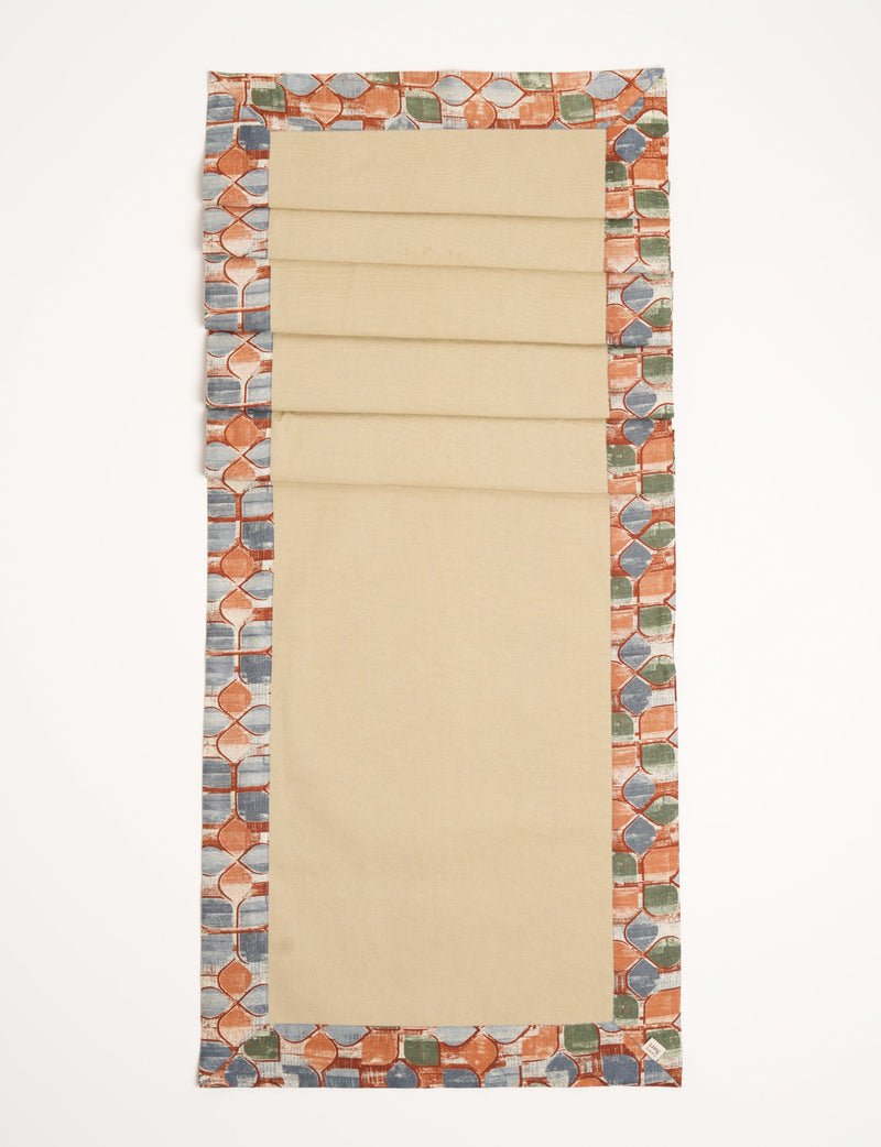 Beige table runner with orange, blue, and green abstract patterned border, flat laid on white background