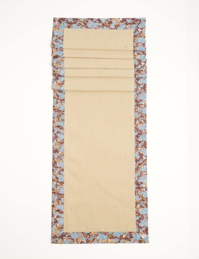 Brown table runner with blue floral border and beige center, flat laid with visible fabric texture and corner label
