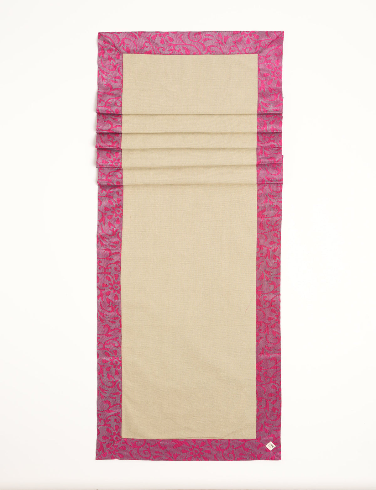 Beige table runner with pink floral patterned border, flat laid with visible fabric texture and a small corner label
