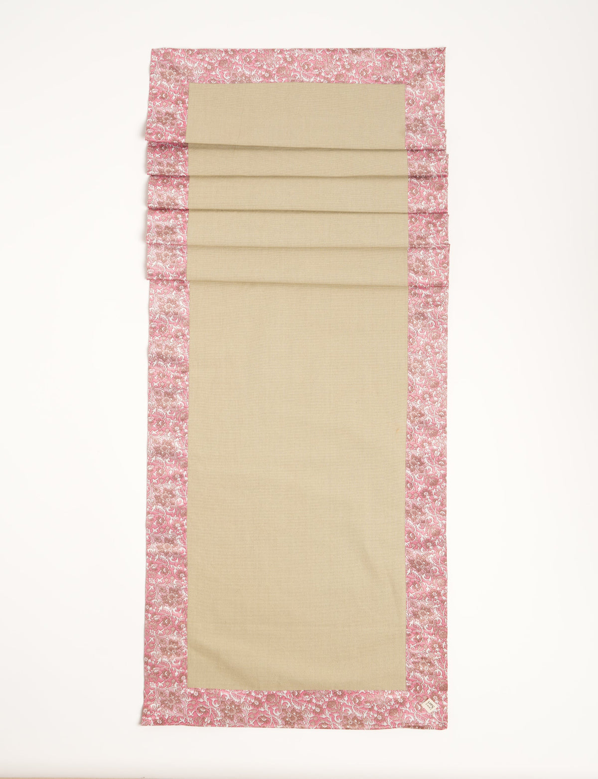 Beige table runner with pink floral ethnic border, flat lay, rectangular shape, fabric texture visible, small label on corner