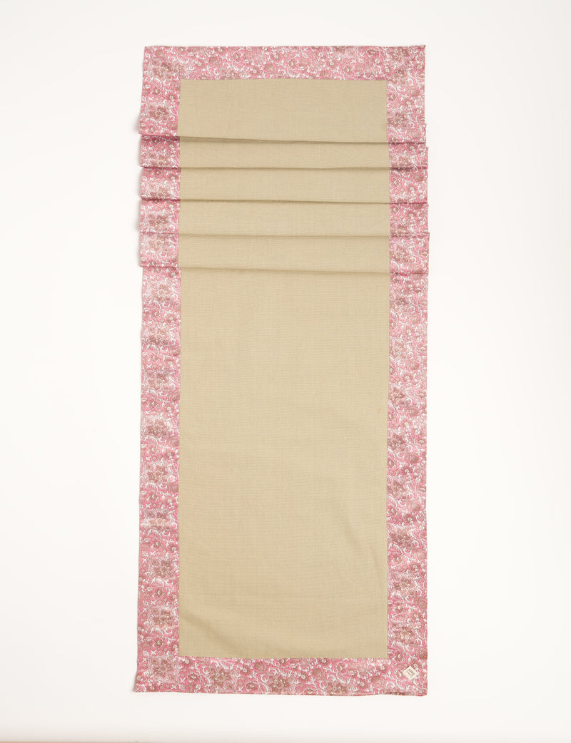 Beige table runner with pink floral ethnic border, flat lay, rectangular shape, fabric texture visible, small label on corner