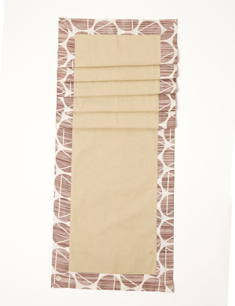 Brown and beige table runner with geometric circle pattern border, flat laid on white background