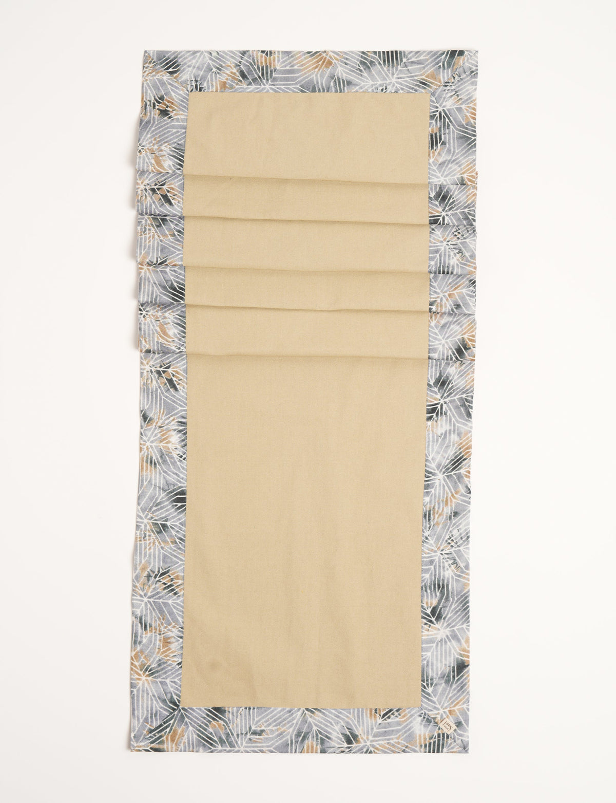 Beige table runner with grey geometric patterned border and small fabric tag on corner, flat lay view