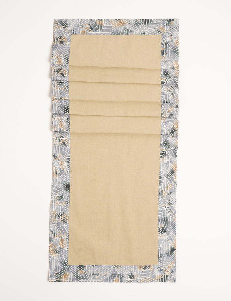 Beige table runner with grey geometric patterned border and small fabric tag on corner, flat lay view