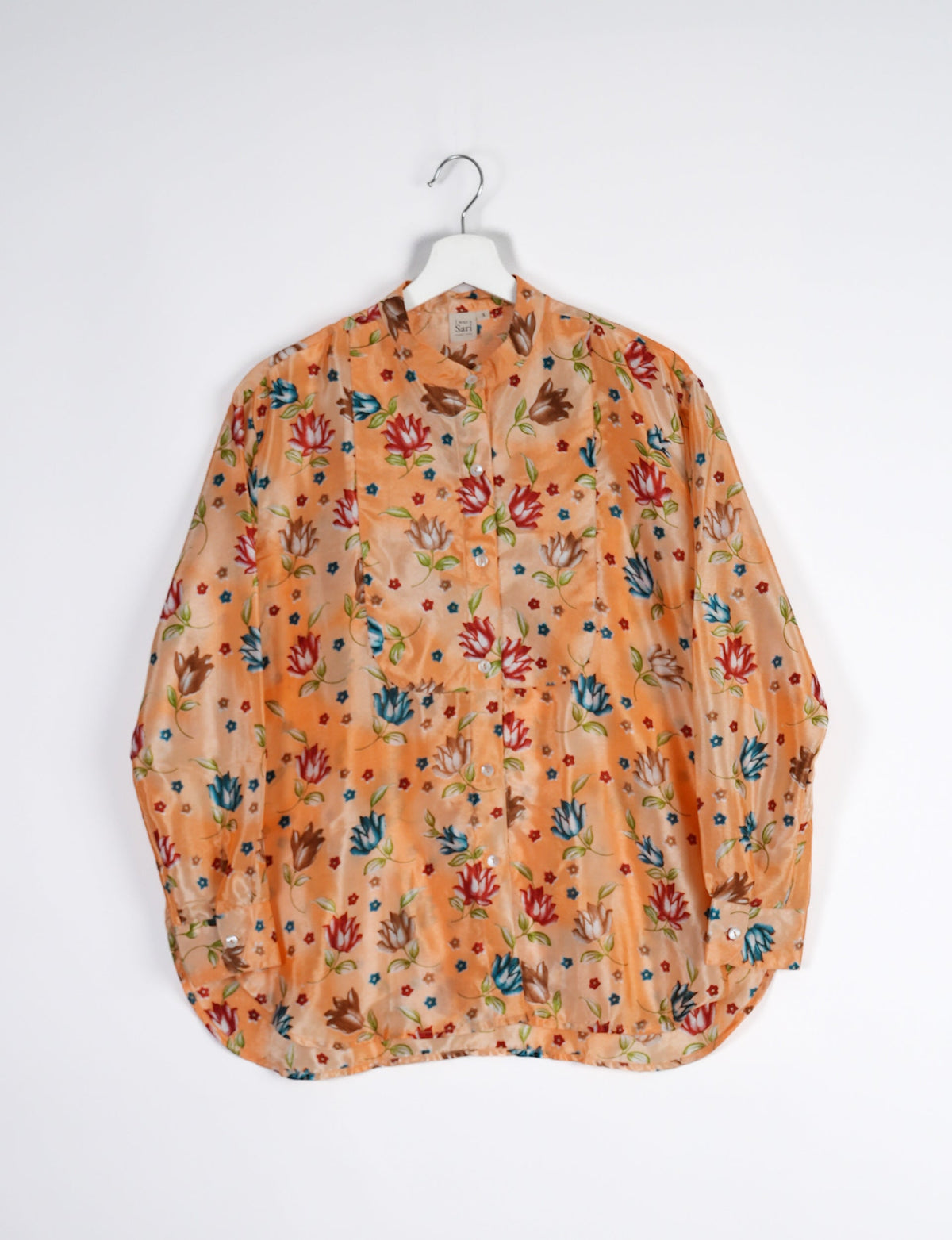 Orange longline button-up shirt with multicolor floral print, mandarin collar, and long sleeves hanging on white hanger