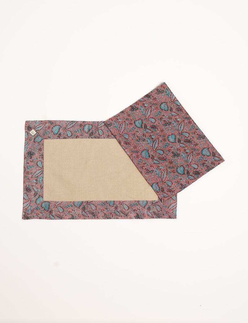 Set of four canvas placemats with red and teal leaf pattern border and beige center, flat lay on white background