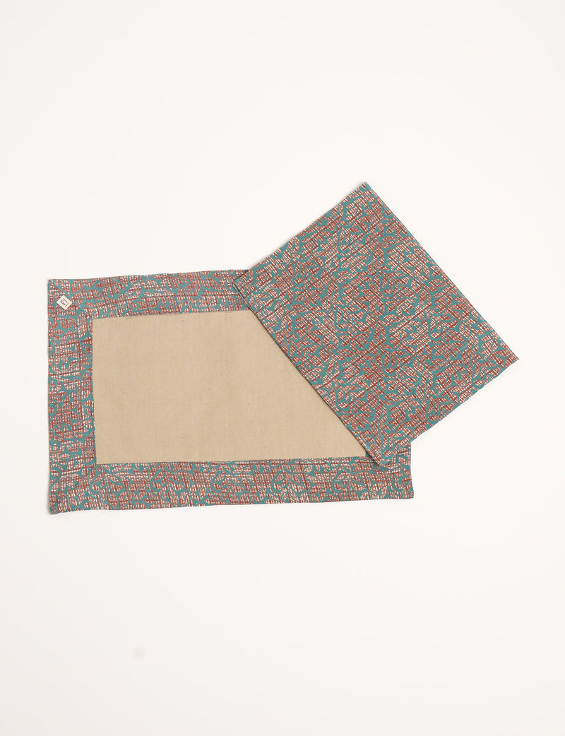 Set of two canvas placemats with brown abstract leaf pattern on teal border and beige center, flat lay view